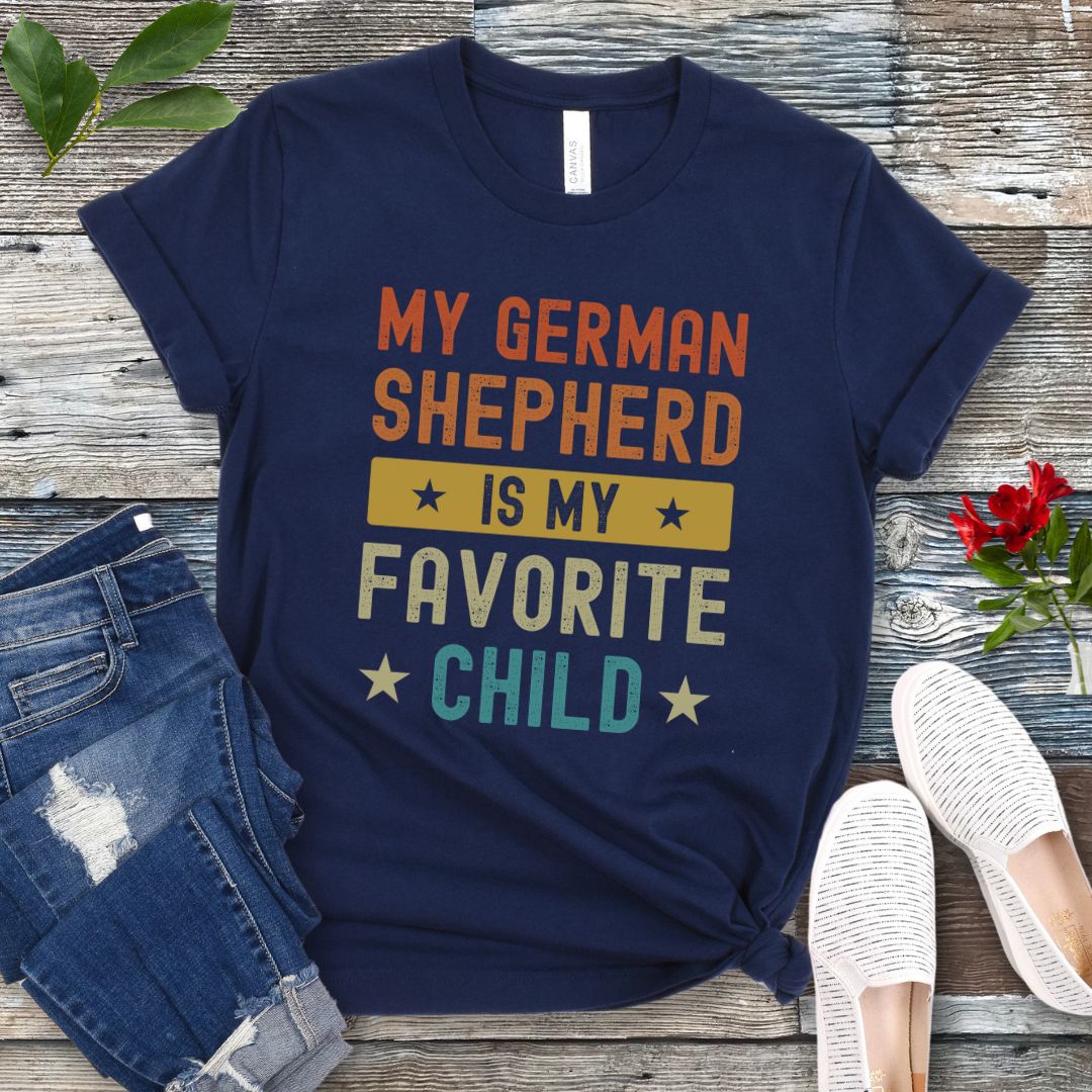Navy blue t-shirt with colorful text 'My German Shepherd is my Favorite Child' on a wooden surface with jeans and shoes.