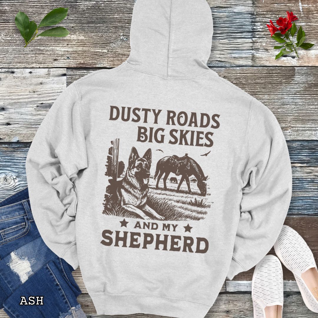 Back view of light grey hoodie featuring a Western-style design with grazing horse, rustic fence, and a German Shepherd illustration; text reads “Dusty Roads, Big Skies, and My Shepherd.”