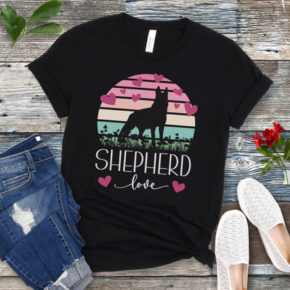 Black t-shirt with pastel vintage sunset, hearts, German Shepherd dog and the text Shepherd Love' in feminine script, presented on a wooden surface with jeans and shoes.
