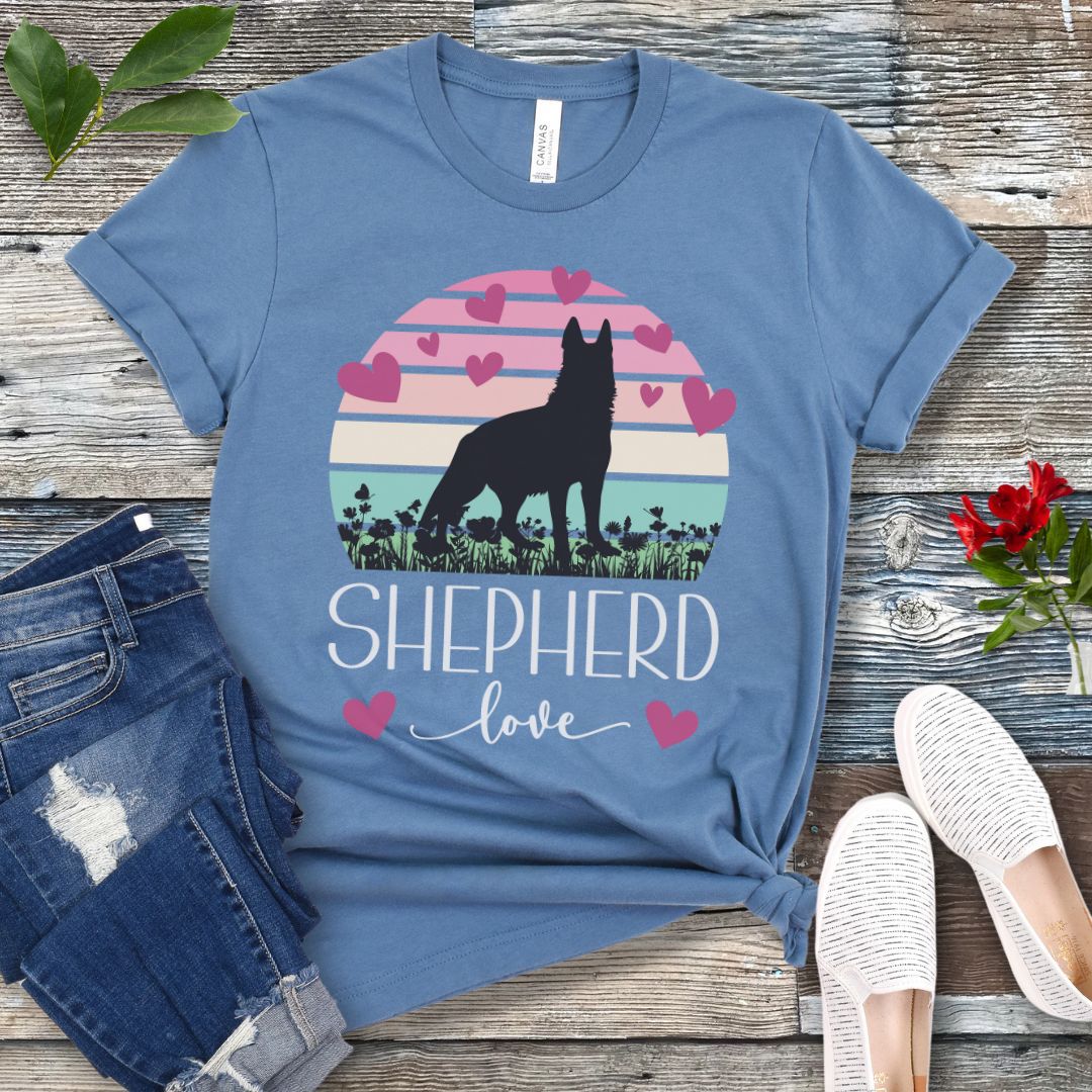 Steel blue t-shirt with pastel vintage sunset, hearts, German Shepherd dog and the text Shepherd Love' in feminine script, presented on a wooden surface with jeans and shoes.