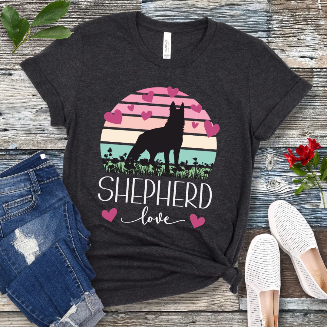 Dark grey t-shirt with pastel vintage sunset, hearts, German Shepherd dog and the text Shepherd Love' in feminine script, presented on a wooden surface with jeans and shoes.