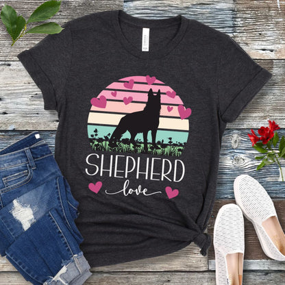 Dark grey t-shirt with pastel vintage sunset, hearts, German Shepherd dog and the text Shepherd Love' in feminine script, presented on a wooden surface with jeans and shoes.