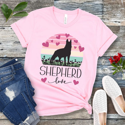 Pink t-shirt with pastel vintage sunset, hearts, German Shepherd dog and the text Shepherd Love' in feminine script, presented on a wooden surface with jeans and shoes.