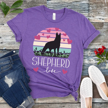 Purple t-shirt with pastel vintage sunset, hearts, German Shepherd dog and the text Shepherd Love' in feminine script, presented on a wooden surface with jeans and shoes.