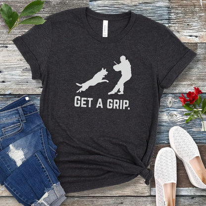 Dark grey t-shirt with bitework graphic of a protection dog and K9 decoy and the text 'GET A GRIP.' on a wooden surface with jeans and shoes.