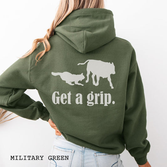 A military green back print hoodie with a graphic of a Heeler dog herding a cow and the text 'Get a grip.' Worn by a person.