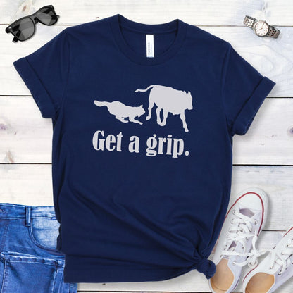 A navy blue t-shirt with a graphic of a dog herding a cow and the humorous text 'Get a grip.' The t-shirt is presented in a casual style with rolled-up sleeves, accompanied by jeans and white shoes.