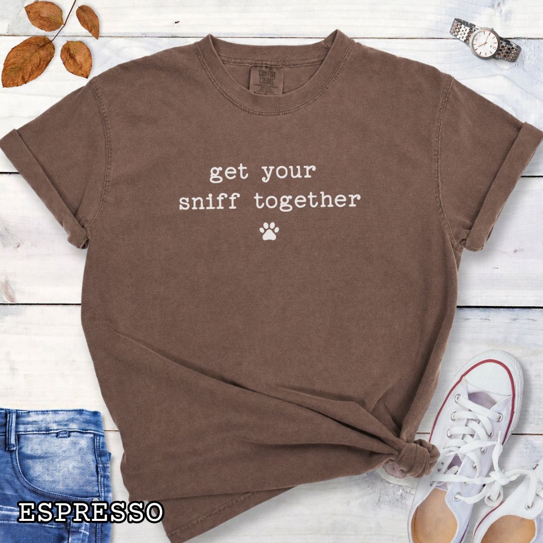 Brown Comfort Colors dog nosework t-shirt with text 'get your sniff together' and paw print on a wooden surface with sunglasses and jeans.