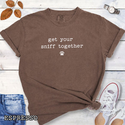 Brown Comfort Colors dog nosework t-shirt with text 'get your sniff together' and paw print on a wooden surface with sunglasses and jeans.