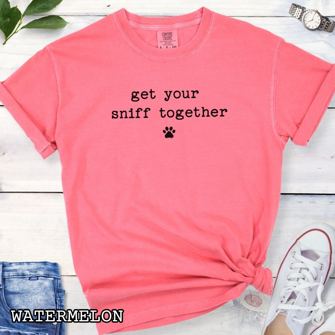 Watermelon color Comfort Colors dog K9 scent work t-shirt with text 'get your sniff together' and paw print on a wooden surface with sunglasses and jeans.