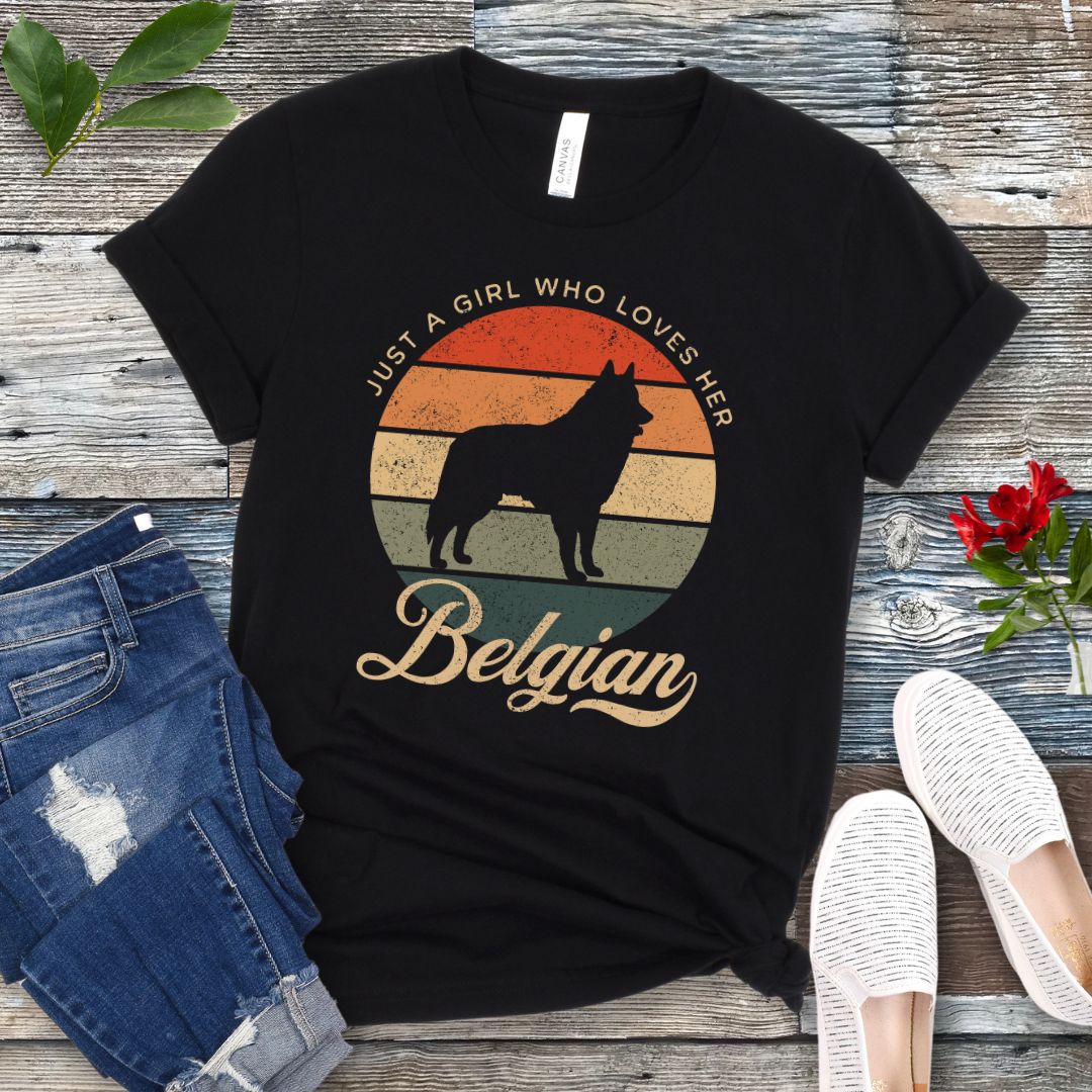 Black t-shirt for Belgian Sheepdog lovers with vintage sunset graphic and Belgian Sheepdog silhouette, and text 'Just a Girl Who Loves Her Belgian', shown on a wooden surface with accessories.
