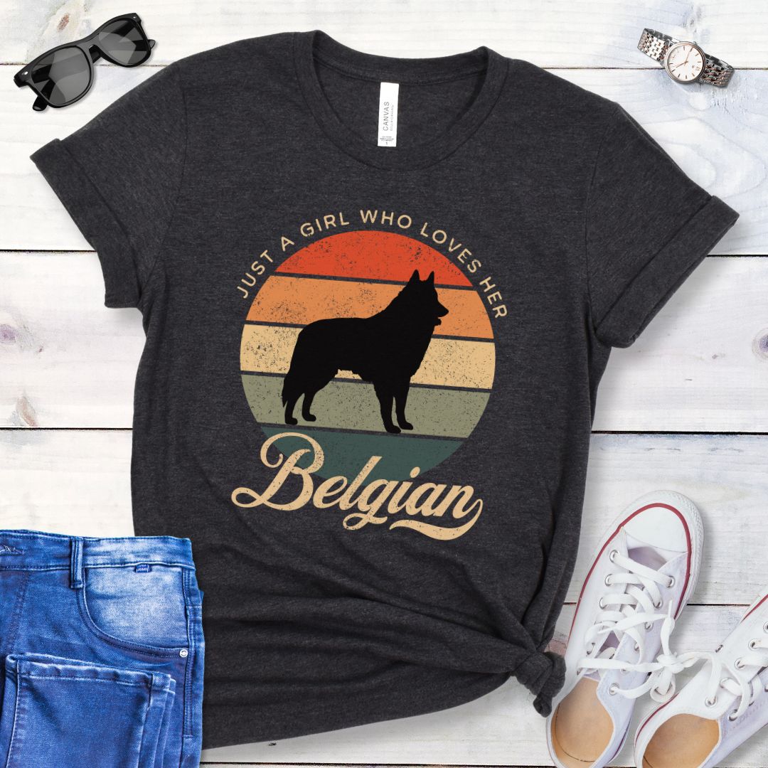 Dark grey t-shirt for Belgian Sheepdog lovers with vintage sunset graphic and Belgian Sheepdog silhouette, and text 'Just a Girl Who Loves Her Belgian', shown on a wooden surface with accessories.