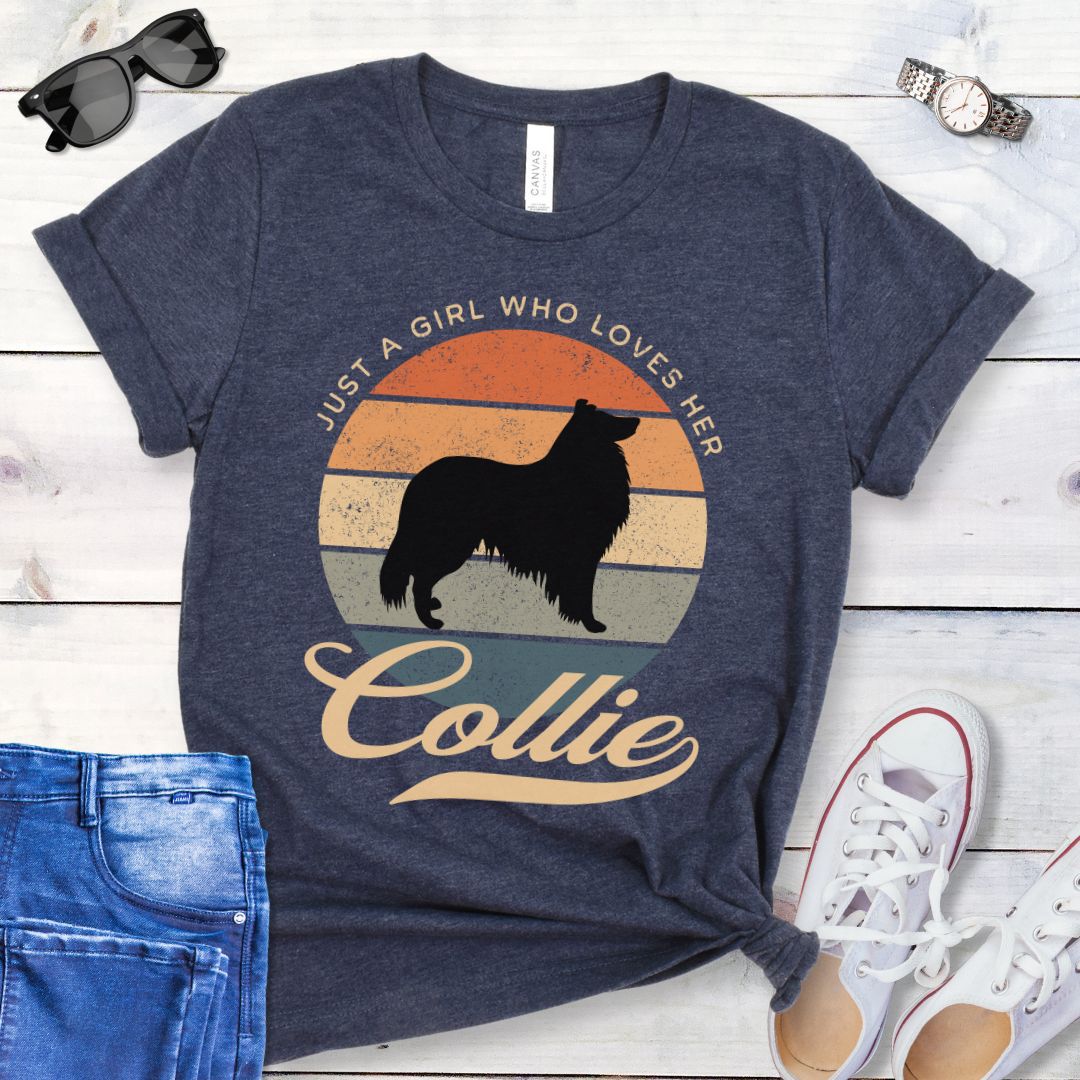 Heather navy Collie mom t-shirt with a vintage sunset design with Rough Collie and the text 'Just a Girl Who Loves Her Collie', shown on a wooden surface with jeans and shoes.