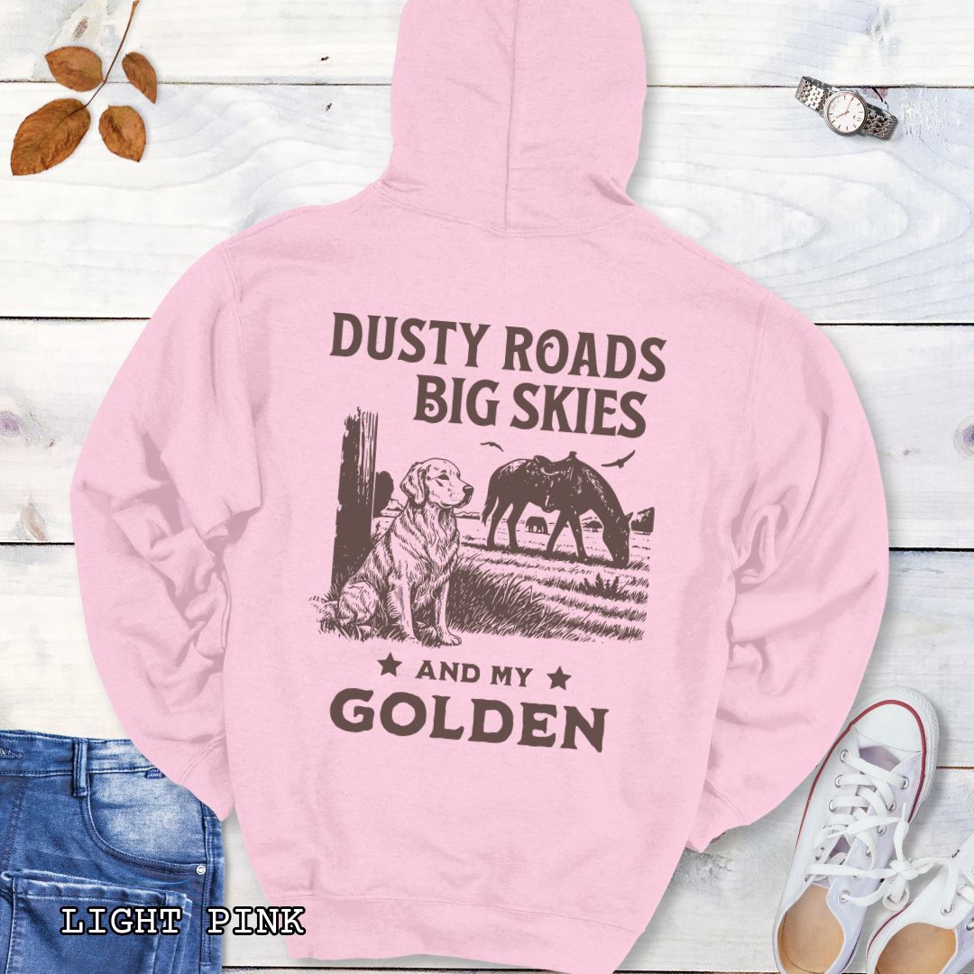 Back view of light pink hoodie featuring a Western-style design with grazing horse, rustic fence, and a Golden Retriever illustration; text reads “Dusty Roads, Big Skies, and My Golden.”