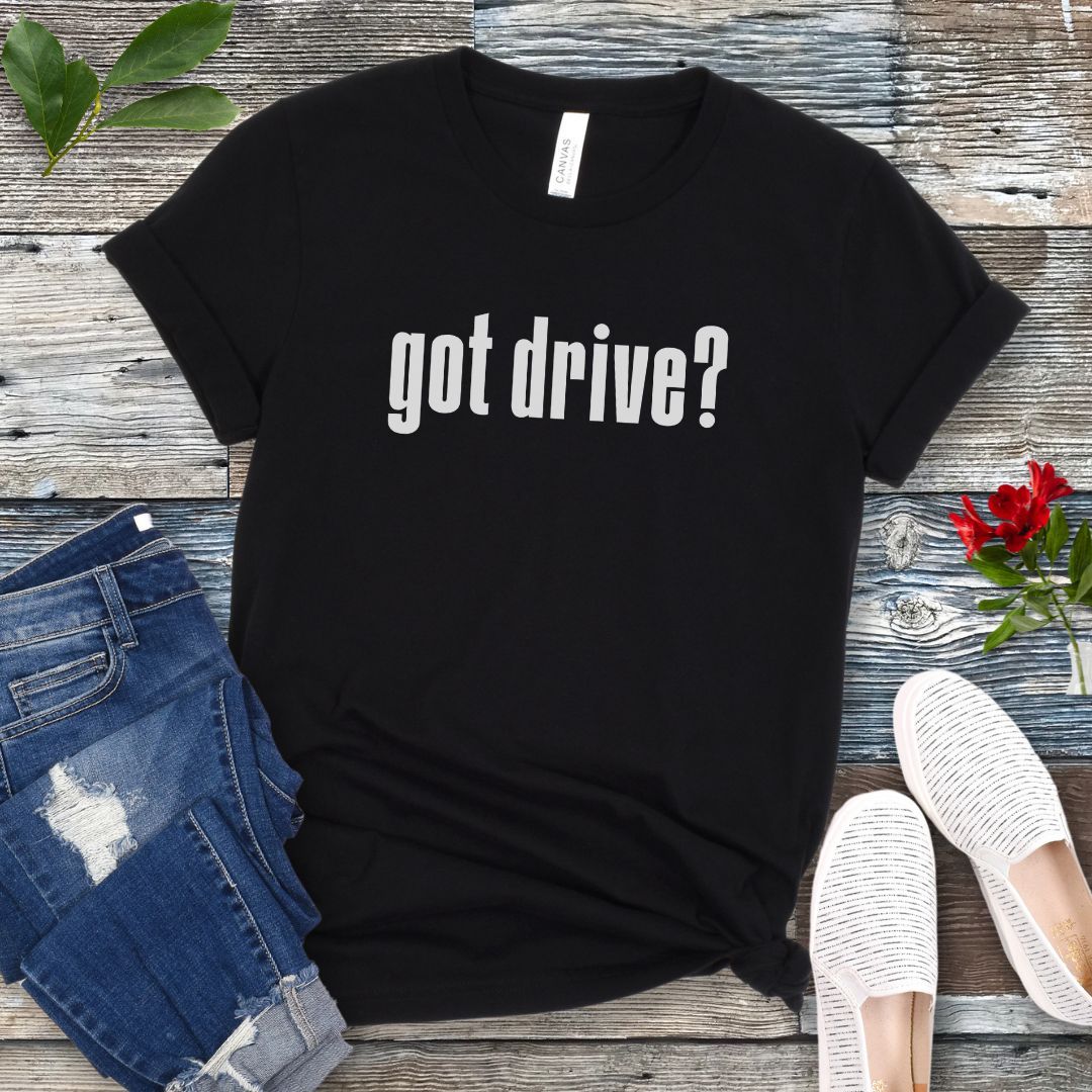 Black IGP dog sports t-shirt with 'got drive?' text on a wooden surface with jeans and shoes.