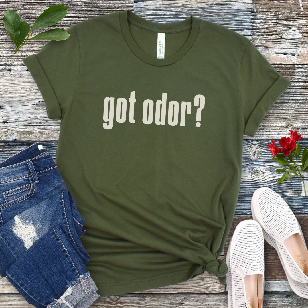 Military green canine scent work t-shirt with 'got odor?' text on a wooden surface with jeans and shoes.