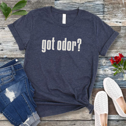 Heather navy dog nosework t-shirt with 'got odor?' text on a wooden surface with jeans and shoes.