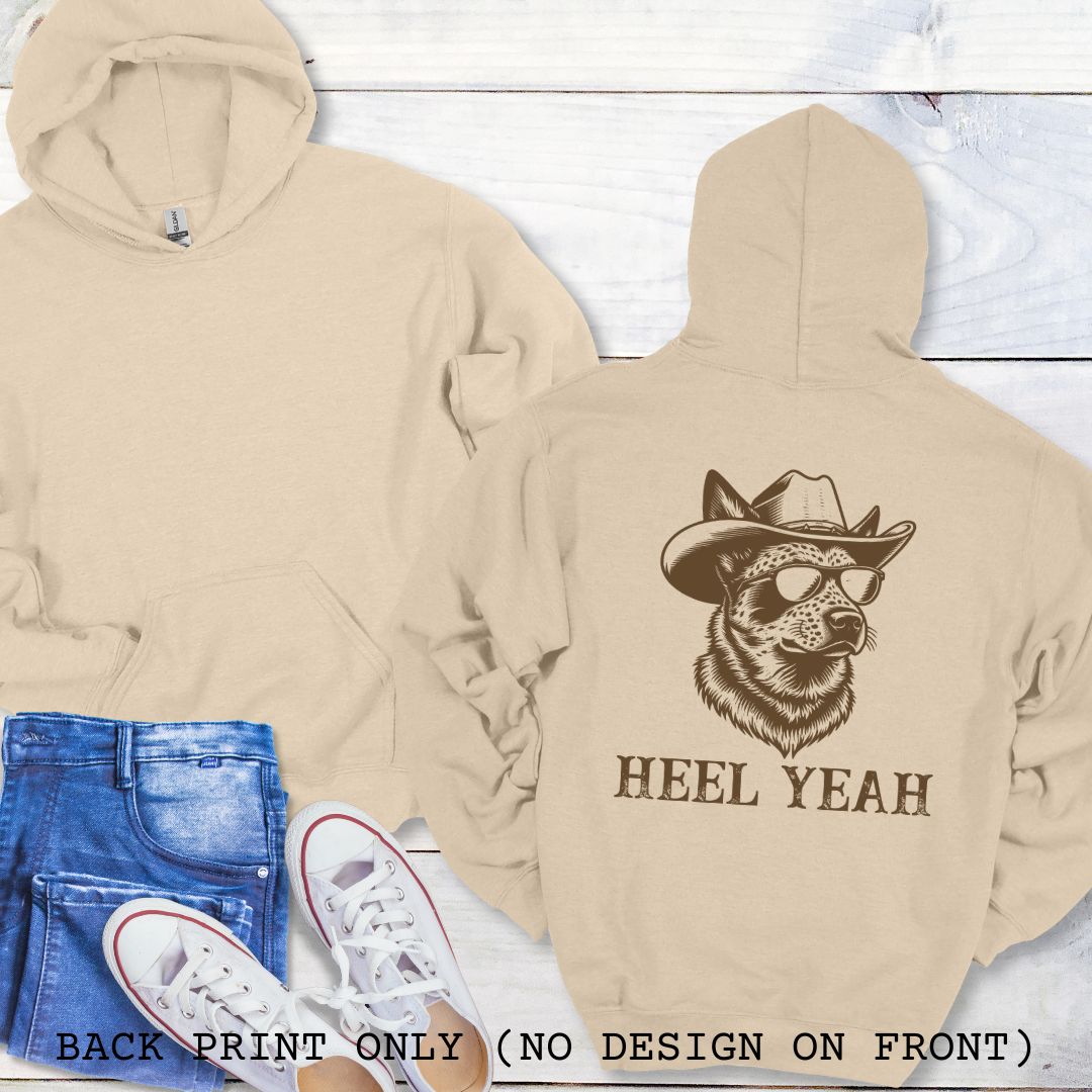 Beige Australian Cattle Dog hoodie with a graphic of a Heeler dog in cowboy hat and sunglasses,  and 'HEEL YEAH' text on the back, presented on a wood surface with accessories.