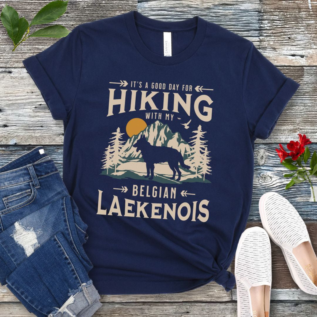 A navy blue t-shirt with a vintage-style graphic print of mountains and a Belgian Laekenois and the text 'Hiking with my Laekenois'. The shirt is presented on a wooden surface with a pair of blue jeans and white shoes in the background.