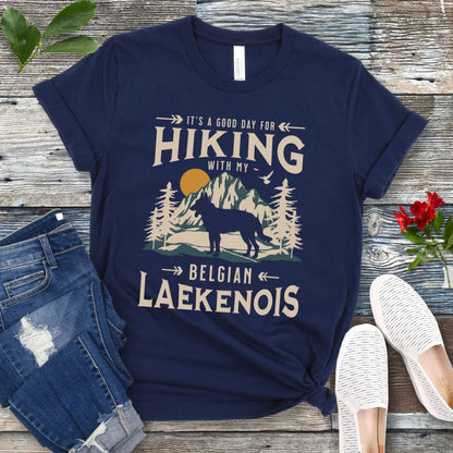 A navy blue t-shirt with a vintage-style graphic print of mountains and a Belgian Laekenois and the text 'Hiking with my Laekenois'. The shirt is presented on a wooden surface with a pair of blue jeans and white shoes in the background.