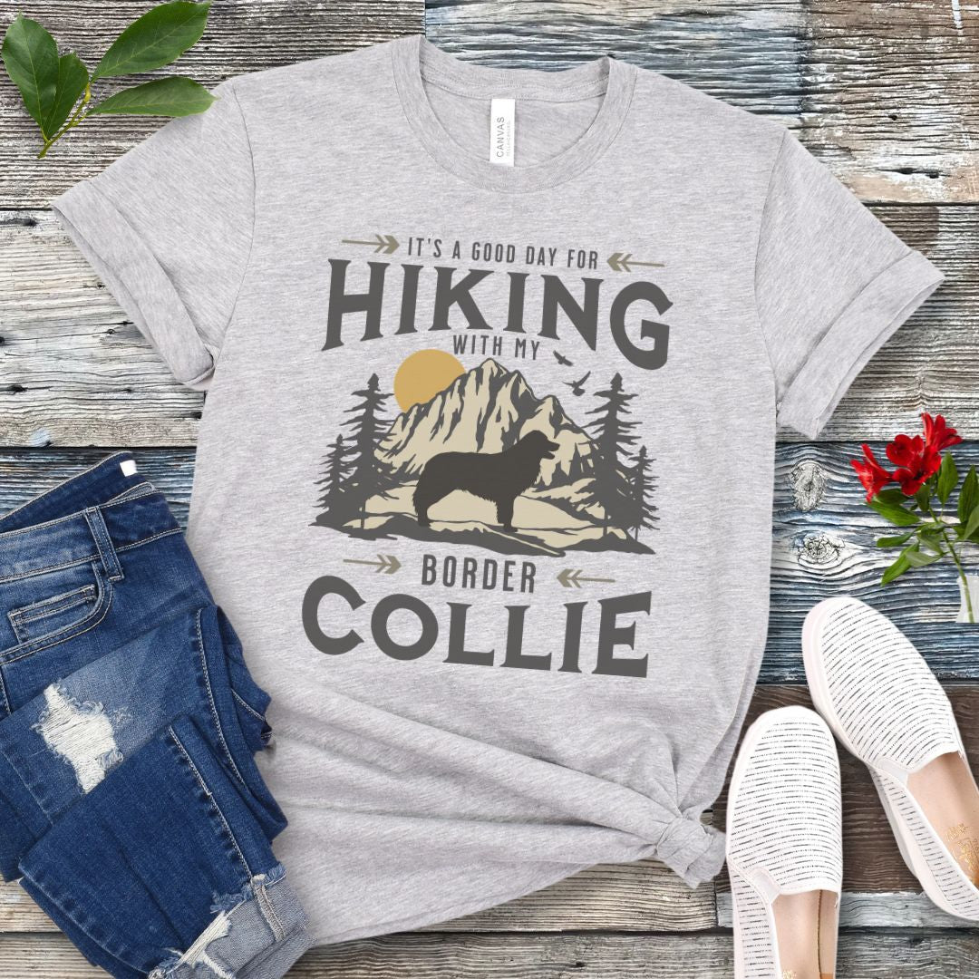 Light grey t-shirt for Border Collie lovers with vintage style mountain graphic and Border Collie silhouette with the text 'It's a Good Day For Hiking With My Border Collie'. Shown on a wooden surface with jeans and shoes.