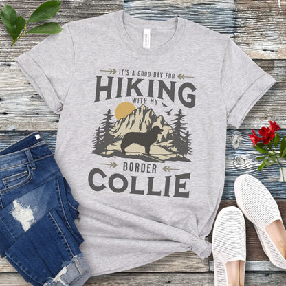 Light grey t-shirt for Border Collie lovers with vintage style mountain graphic and Border Collie silhouette with the text 'It's a Good Day For Hiking With My Border Collie'. Shown on a wooden surface with jeans and shoes.