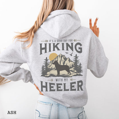 A light grey back print hoodie with a graphic print of a Cattle Dog and vintage mountains illustration, and text that reads 'HIKING WITH MY HEELER'. 
