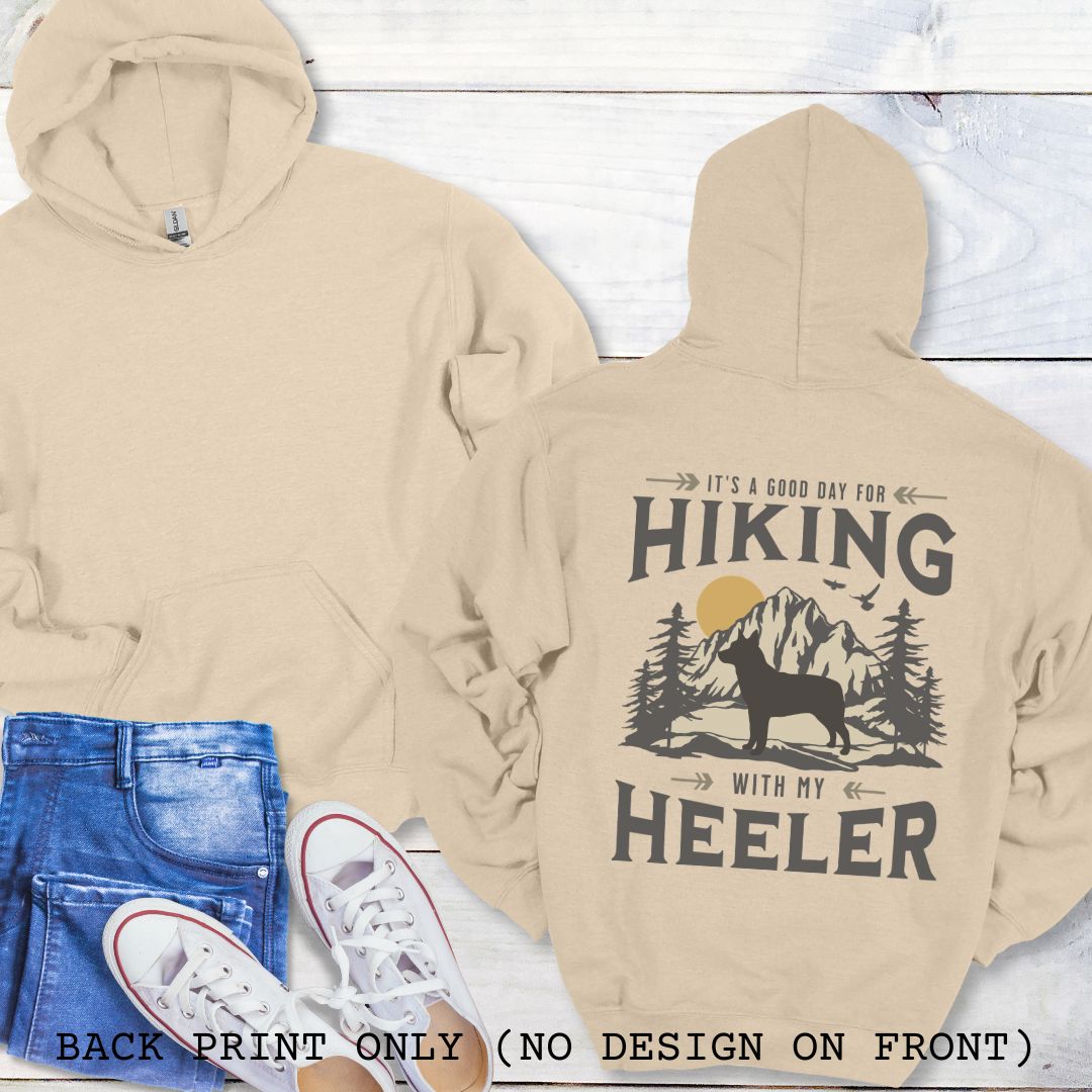A beige back print hoodie with a graphic print of a Cattle Dog and vintage mountains illustration, and text that reads 'HIKING WITH MY HEELER'. 