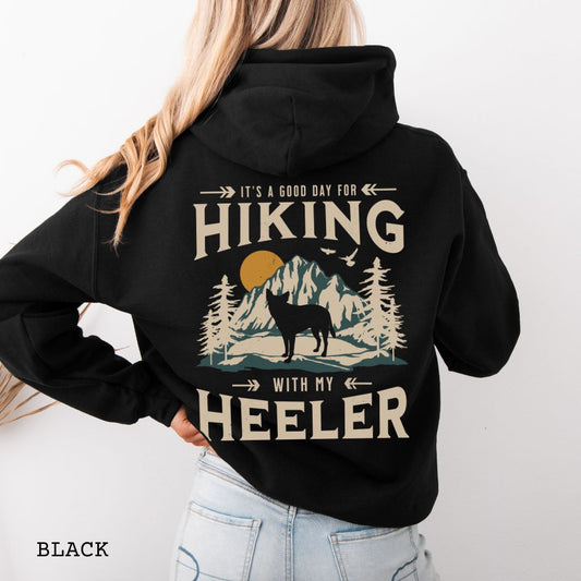 Black back print dog lover hoodie with vintage mountain graphic, Australian Heeler and 'It's a Good Day for Hiking With My Heeler' text, worn by a person.
