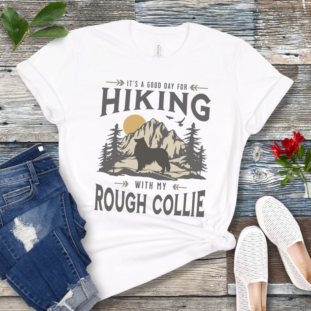 White Collie lover t-shirt with vintage mountain scene graphic, a rough collie silhouette and text 'It's a Good Day For Hiking With My Rough Collie', shown on a wooden surface with jeans and shoes.