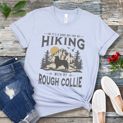 Light blue Collie lover t-shirt with vintage mountain scene graphic, a rough collie silhouette and text 'It's a Good Day For Hiking With My Rough Collie', shown on a wooden surface with jeans and shoes.