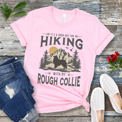 Pink Collie lover t-shirt with vintage mountain scene graphic, a rough collie silhouette and text 'It's a Good Day For Hiking With My Rough Collie', shown on a wooden surface with jeans and shoes.