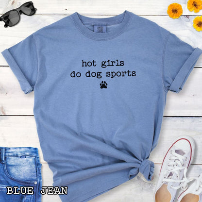 Blue Comfort Colors t-shirt for dog agility, nosework, barn hunt, and flyball lovers, with humorous text 'hot girls do dog sports', shown on a wooden surface with jeans and shoes. 