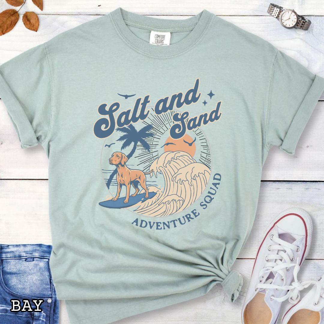 Light green Comfort Colors t-shirt for Hungarian Vizsla dog lovers with retro surfing Vizsla graphic in a beach setting with 'Salt and Sand Adventure Squad' text, shown on a wooden surface.