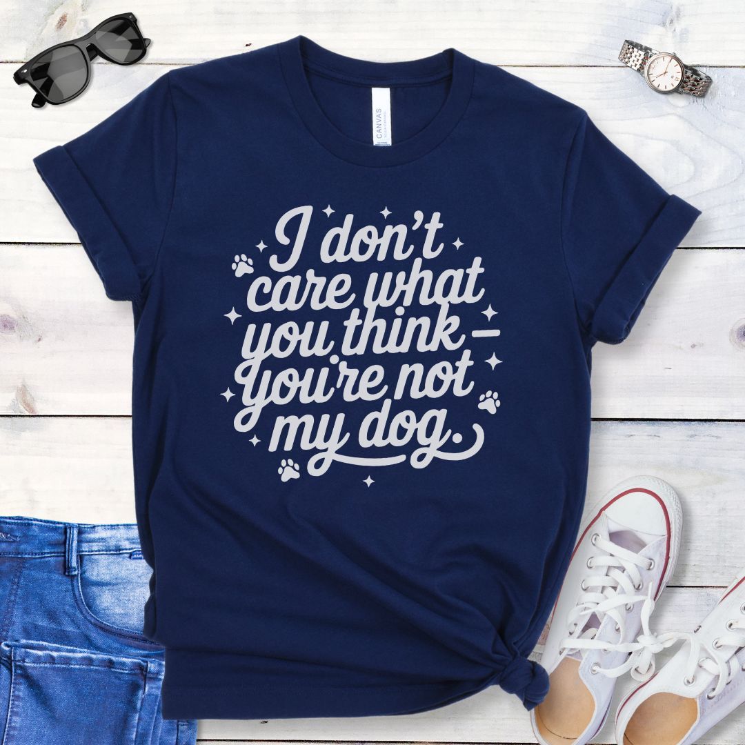 A navy colored dog lover t-shirt with the typography text 'I don't care what you think you're not my dog' printed on it, accented by stars and paw prints, displayed flat with a pair of blue jeans and white shoes.