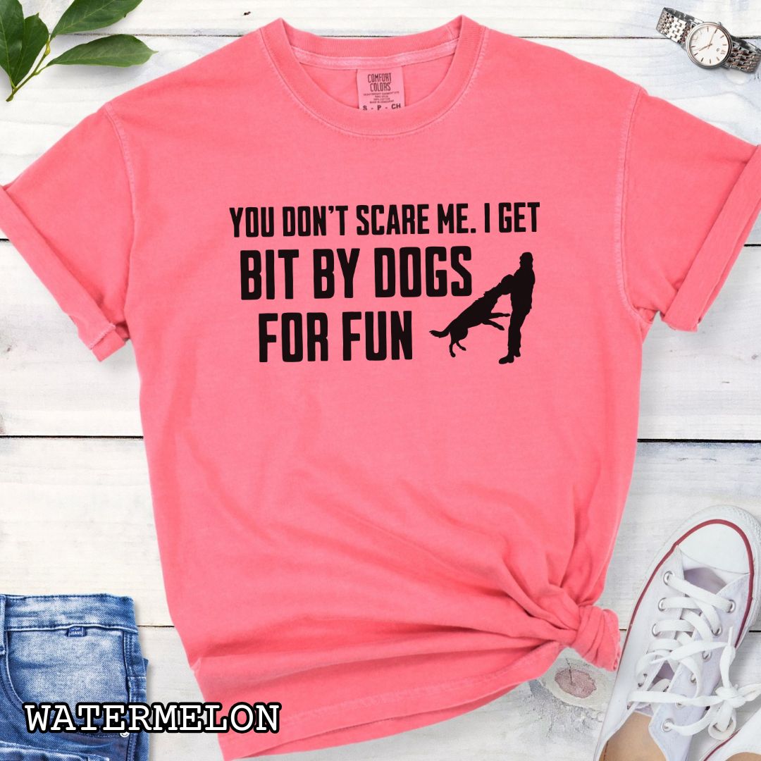 Pink Comfort Colors t-shirt featuring the phrase You Don't Scare Me. I Get Bit by Dogs for Fun with K9 bite work silhouette, funny Schutzhund shirt for IGP decoys, Schutzhund helpers, working dog handlers, protection sports enthusiasts, and IPO competitors.