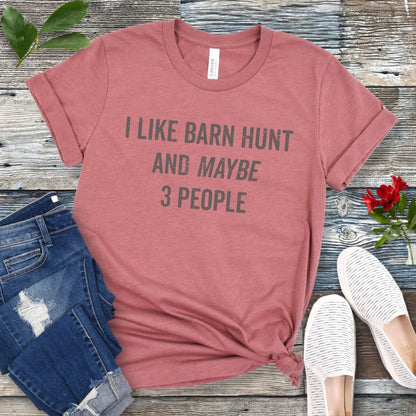 Mauve t-shirt with text 'I LIKE BARN HUNT AND MAYBE 3 PEOPLE' on a wooden surface with jeans and shoes.