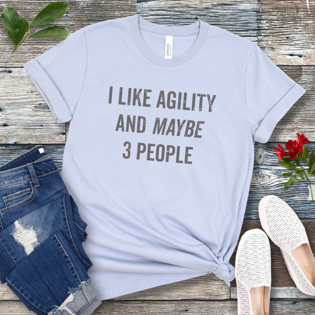 Light blue t-shirt with 'I LIKE AGILITY AND MAYBE 3 PEOPLE' text on a wooden surface with jeans and shoes.