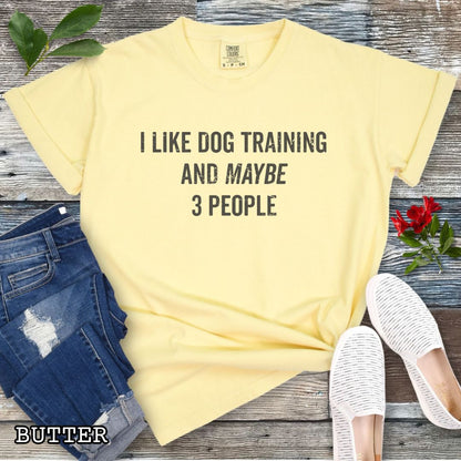 Yellow (Butter) Comfort Colors t-shirt with 'I like dog training and maybe 3 people' text, presented on a wooden surface with shoes and jeans.