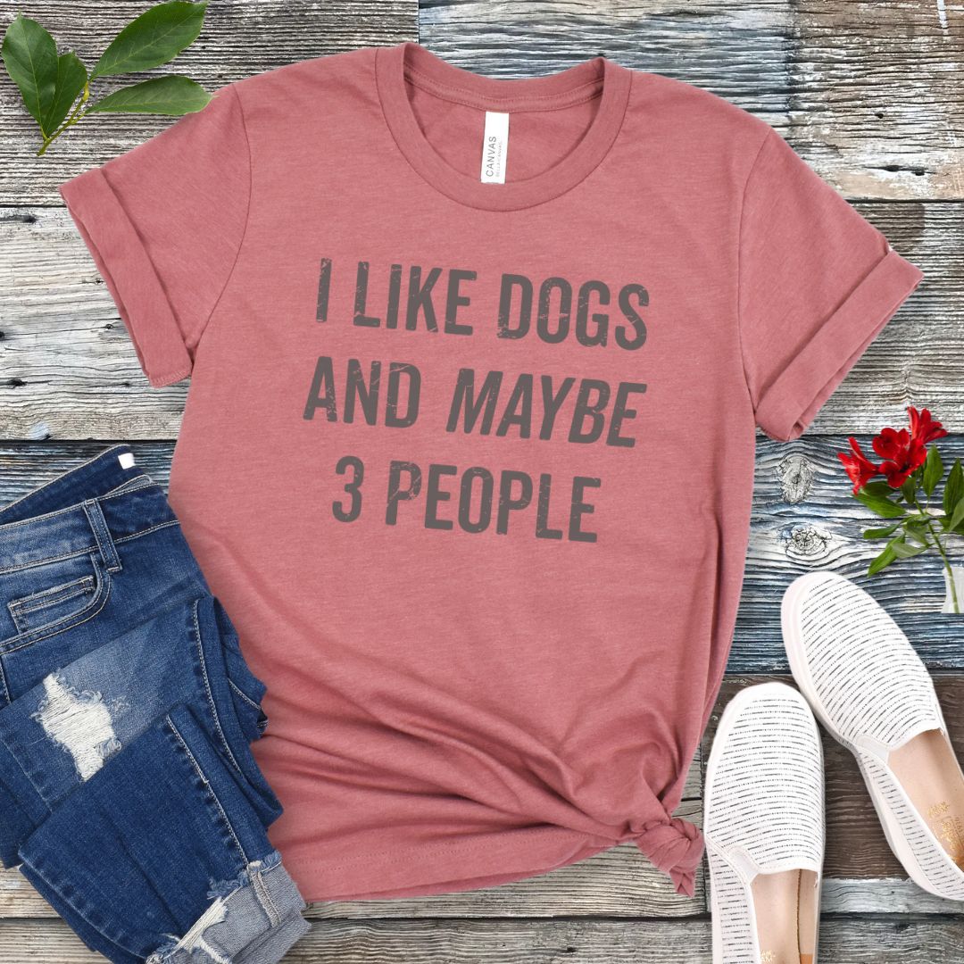 Mauve t-shirt with 'I like dogs and maybe 3 people' text on a wooden surface with jeans and shoes.