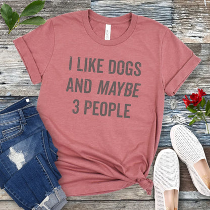 Mauve t-shirt with 'I like dogs and maybe 3 people' text on a wooden surface with jeans and shoes.