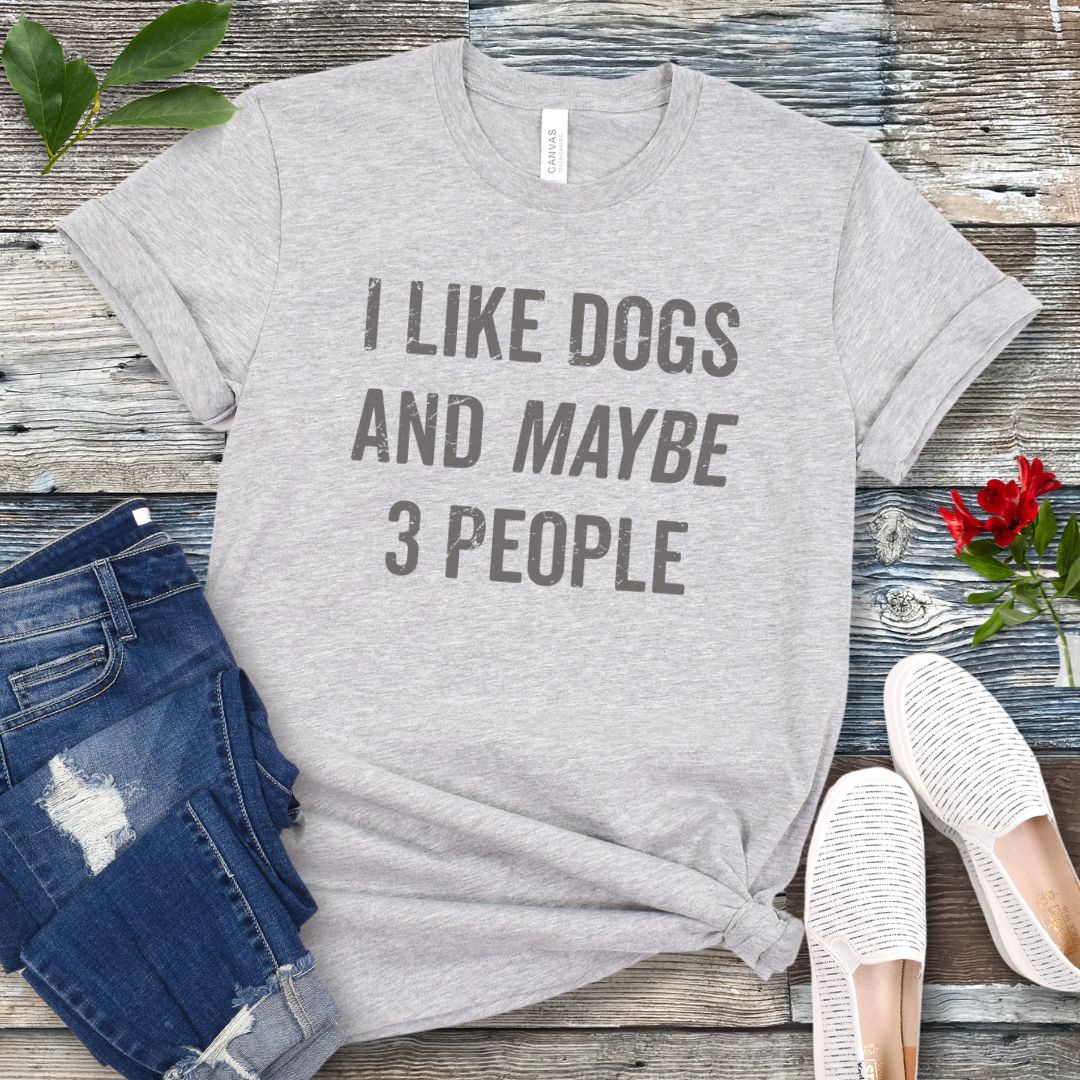 Gray t-shirt with 'I Like Dogs And Maybe 3 People' text on a wooden surface with jeans and shoes.