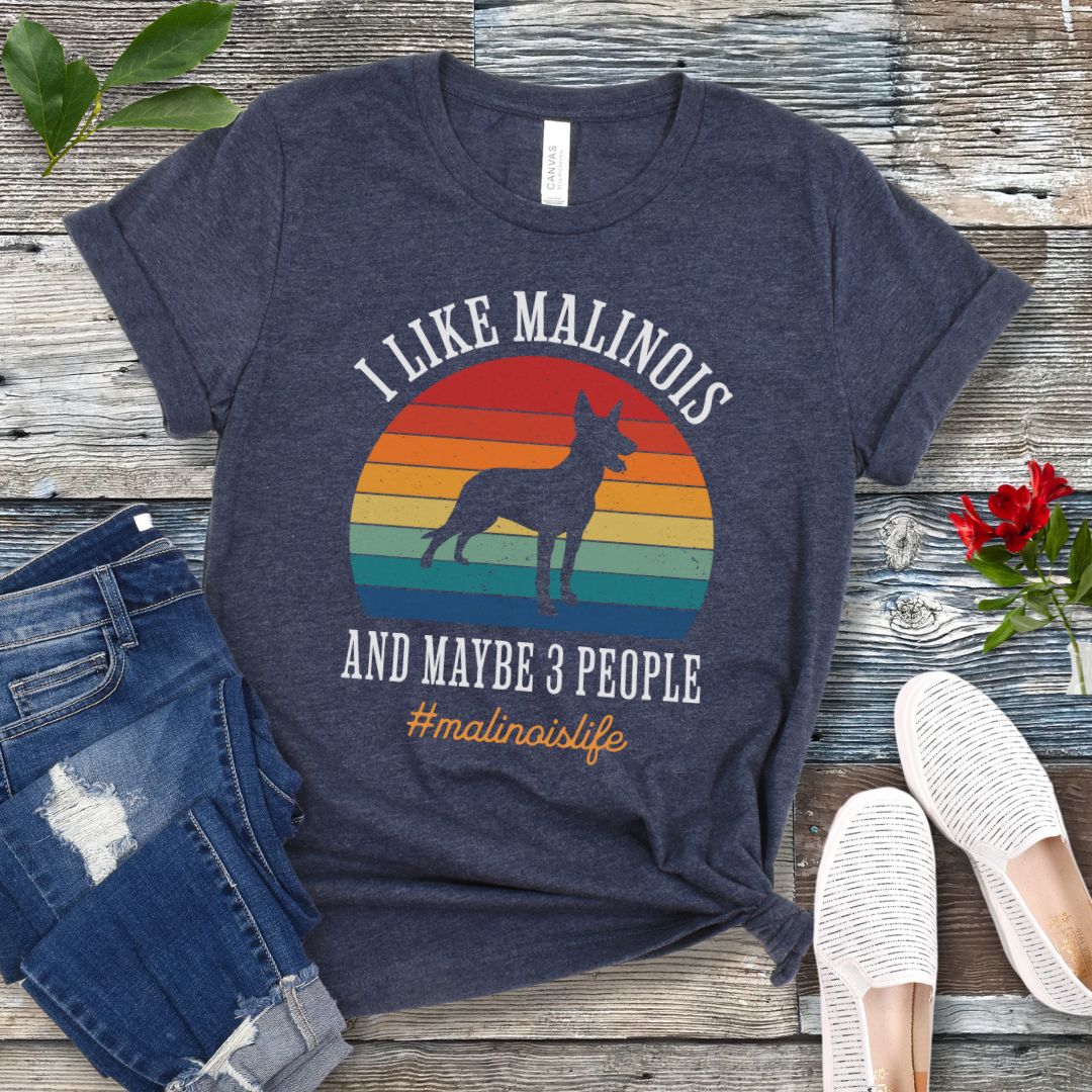 Heather navy t-shirt with Belgian Malinois dog graphic, vintage sunset and the text 'I like Malinois and maybe 3 people. #malinoislife', presented on a wooden surface with jeans and shoes.