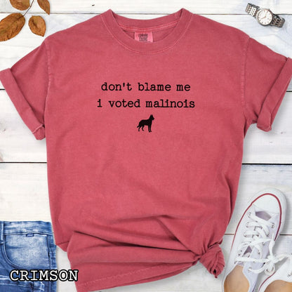 Red Comfort Colors t-shirt for Belgian Malinois lovers with humorous text, 'don't blame me, i voted malinois' and dog graphic, shown on a wooden surface with accessories.