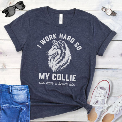 Heather navy blue unisex t-shirt for Rough Collie lovers with linocut-style breed head study graphic and humorous text 'I work hard so my Collie can have a better life', shown on a wooden surface with jeans and shoes. 