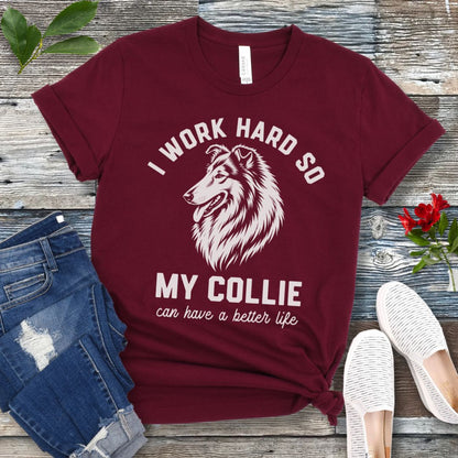 Maroon unisex t-shirt for Rough Collie lovers with linocut-style breed head study graphic and humorous text 'I work hard so my Collie can have a better life', shown on a wooden surface with jeans and shoes. 