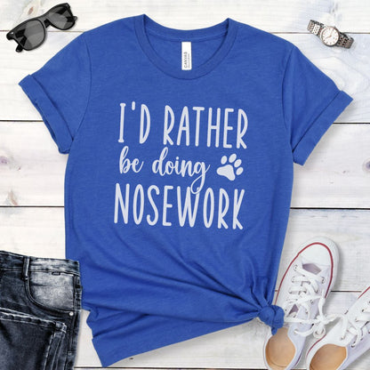 Royal blue t-shirt for K9 nose work dog trainers with 'I'd rather be doing nosework' text on a wooden surface with accessories.