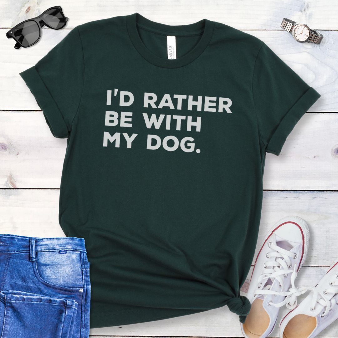 Dark green t-shirt for dog lovers with 'I'd Rather Be With My Dog' text in bold lettering, shown on a wooden surface with jeans and shoes.