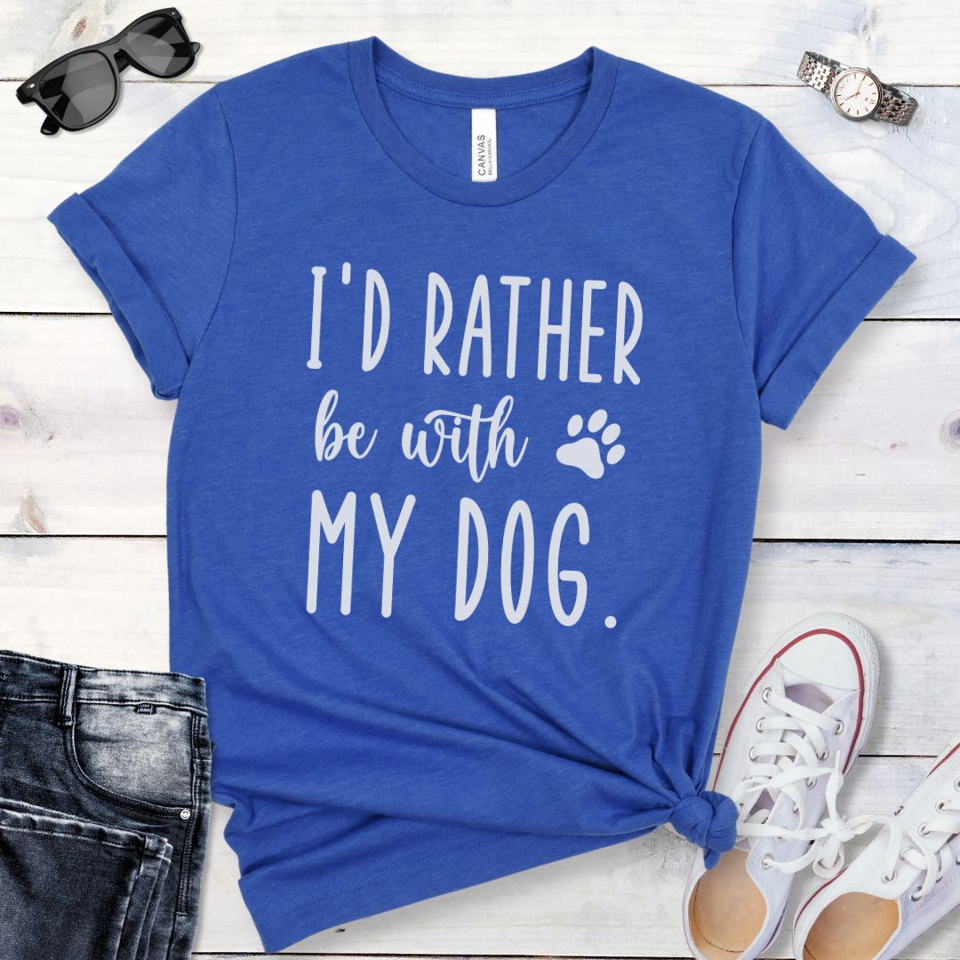 Royal blue t-shirt for dog lovers and dog moms with the humorous text 'I'd rather be with my dog' in playful, handwritten font, shown on a wooden surface with jeans and shoes.