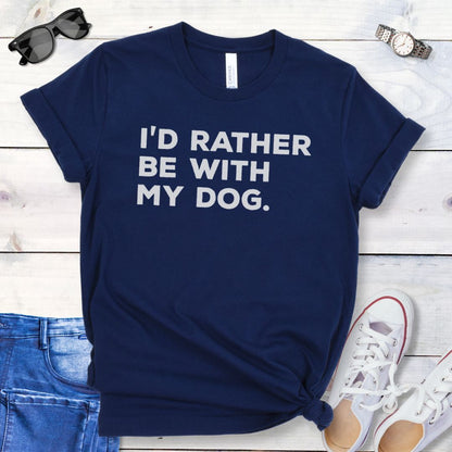 Navy t-shirt for dog people with 'I'd Rather Be With My Dog' text in bold lettering, shown on a wooden surface with jeans and shoes.